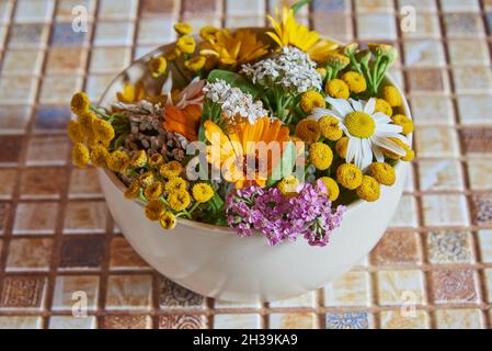 Auf der Arbeitsplatte befindet sich eine Keramikschale mit Heilkräutern und Blumen. Alternative Medizin. Stockfoto
