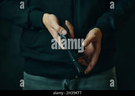 Nahaufnahme der Waffe nachladen. Herrenhände prüfen im Revolverfass auf Kugeln. Kerl in Jeans und schwarzem Hoodie bereitet Pistole auf Schüsse vor. Schusswaffe zur Verteidigung oder zum Angriff. Stockfoto