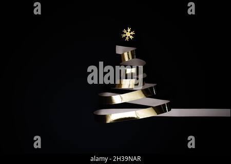 Weihnachtsfeier oder Silvesterkonzept: Weihnachtsbaum aus glänzendem Goldband oder goldenem Streamer vor schwarzem Hintergrund. Stockfoto