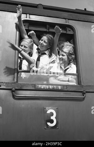 BDM Mädel winken aus ihrer Zugteilfenster bei der Fahrt in die Ferien, Deutschland 1930er Jahre. BDM-Mädchen jubeln aus dem Fenster ihres Zuges, der sie zu ihren Ferien bringt, Deutschland in den 1930er Jahren. Stockfoto