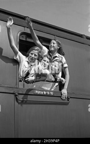 BDM Mädel winken aus ihrer Zugteilfenster bei der Fahrt in die Ferien, Deutschland 1930er Jahre. BDM-Mädchen jubeln aus dem Fenster ihres Zuges, der sie zu ihren Ferien bringt, Deutschland in den 1930er Jahren. Stockfoto