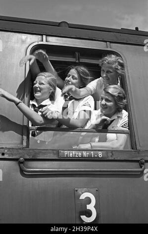 BDM Mädel winken aus ihrer Zugteilfenster bei der Fahrt in die Ferien, Deutschland 1930er Jahre. BDM-Mädchen jubeln aus dem Fenster ihres Zuges, der sie zu ihren Ferien bringt, Deutschland in den 1930er Jahren. Stockfoto