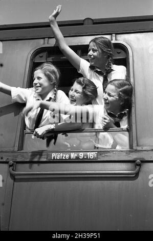 BDM Mädel winken aus ihrer Zugteilfenster bei der Fahrt in die Ferien, Deutschland 1930er Jahre. BDM-Mädchen jubeln aus dem Fenster ihres Zuges, der sie zu ihren Ferien bringt, Deutschland in den 1930er Jahren. Stockfoto