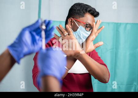 Selektive Fokussierung auf einen Mann mit medizinischer Gesichtsmaske, der Nein zur Covid-19- oder Coronavirus-Impfung sagt, indem er dem Arzt Handgesten zeigt - Konzept des Impfstoffs Stockfoto