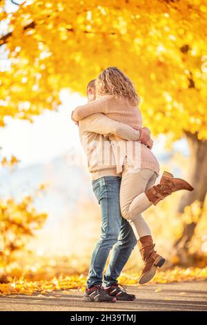 Ein Mann hält im Herbstpark eine Frau in einer Umarmung mit Küssen in den Armen. Stockfoto