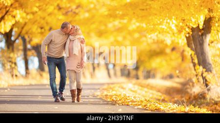 Ein erwachsenes Paar, das in Küsse verliebt ist und durch einen wunderschönen Herbstpark läuft. Stockfoto