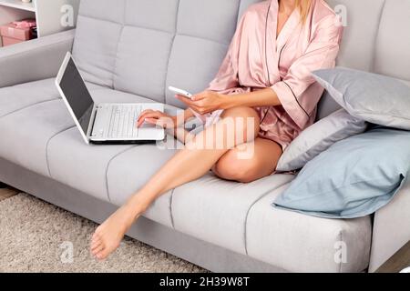 Frau, die zu Hause im Wohnzimmer Telefon und Laptop benutzt Stockfoto