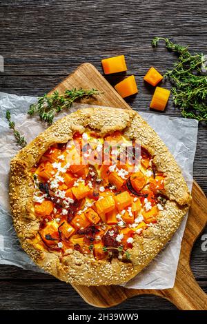 butternut-Kürbisgalette mit karamellisierten Zwiebeln und zerbröseltem Fetakäse auf einem Brett auf einem rustikalen Holztisch, vertikale Ansicht Stockfoto