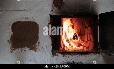 Ein Feuer brennt in Einem Ziegeldorf Ofen. Flammen, heiße Kohlen und Protokolle. Stockfoto