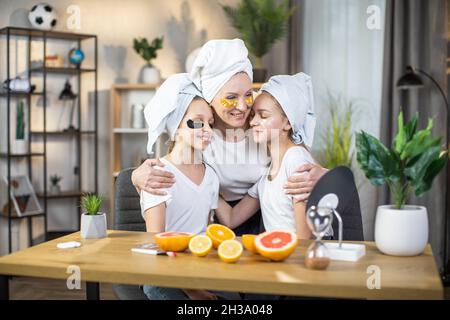 Schöne reife Frau und zwei Teenager-Mädchen mit Handtuch auf dem Kopf Anwendung Kollagen Pads unter den Augen. Mutter mit Töchtern, die zu Hause Zeit für Schönheitsbehandlungen verbringen. Stockfoto