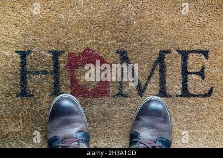 Abgenutzte Stiefel stehen auf einer alten Fußmatte mit Wort zu Hause Stockfoto