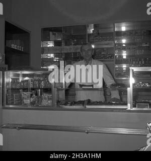 Ein junger Mann an der Theke seiner Konditorei, Deutschland 1950er Jahre. Ein junger Mann an der Theke seines Cafés, Deutschland der 1950er Jahre. Stockfoto
