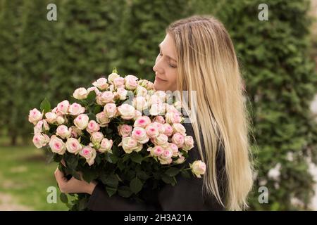 Mädchen hält Blumen in den Händen. Mädchen suchen Strauß. Strauß Rosen Hände des Mädchens. Blumenstrauß. Blumenstrauß. Blumenarrangement von lebendiger Farbe Stockfoto