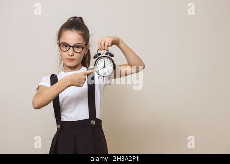 Mädchen mit Wecker. Mädchen zeigt ihren Finger auf die Uhr. Platz für Text Stockfoto