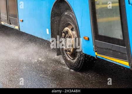 Blauer Stadtbus, der auf einer regnerischen Straße mit Wasserspritzern fährt Stockfoto