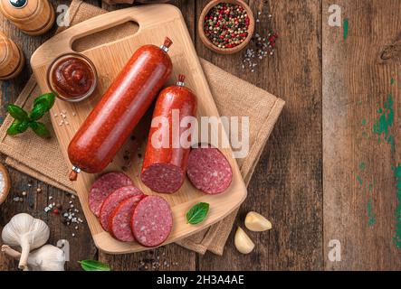 Wurst mit Soße und Knoblauch auf einem Schneidbrett auf einem hölzernen Hintergrund. Stockfoto