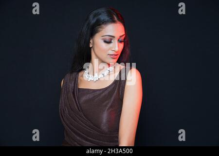 Frau Gesicht Nahaufnahme Porträt. Junge weibliche Model schaut nach unten mit weichem rotem Licht auf dem Gesicht. Schwarzer Hintergrund Stockfoto