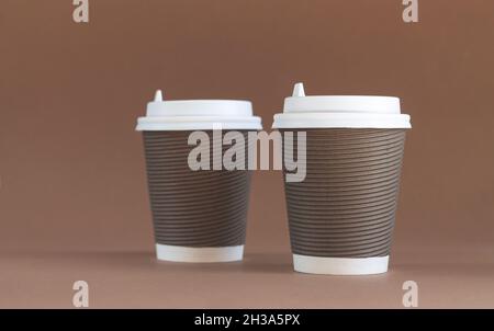 Zwei Pappbecher aus Wellpappe mit Kappen auf braunem Hintergrund mit Platz für Kopien Stockfoto