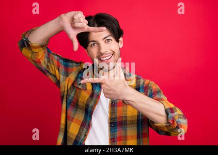 Foto von funky süßen jungen Gentleman tragen karierte Outfit lächelnd zeigen Foto-Shoot Geste isoliert roten Hintergrund Stockfoto