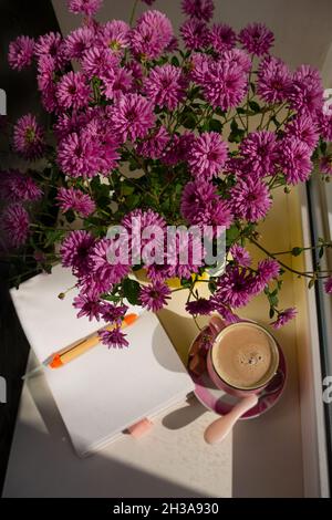Kaffeetasse Schokolade Notizbuch schöne rosa Herbst Chrysantheme Blumen in gelben Topf auf Fenster. Gemütliches Zuhause Stockfoto
