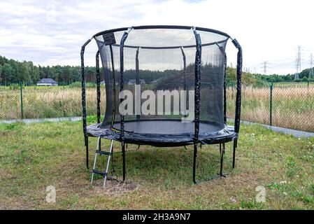 Großes Kinderspringtrampolin mit Schutznetz und geschlossenem Reißverschluss, im Garten stehend. Stockfoto