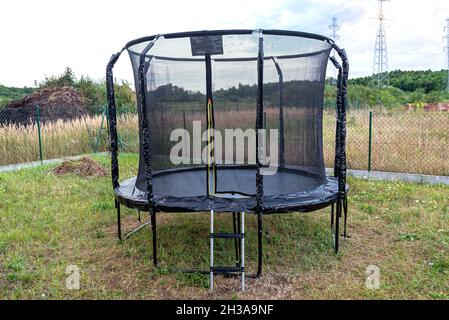 Großes Kinderspringtrampolin mit Schutznetz und offenem Reißverschluss, im Garten stehend. Stockfoto