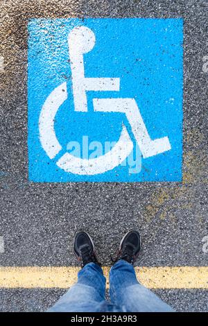 Ein Mann, der vor dem Symbol auf dem Kopfsteinpflaster in dem Bereich steht, der für das Parken von Autos für behinderte Menschen reserviert ist Stockfoto