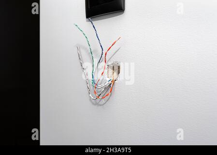 Acht farbige Kabel von der Gegensprechanlage ragen aus der Wand des Hauses im Raum heraus. Stockfoto