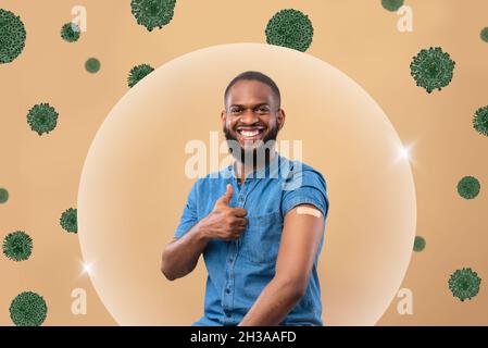 Lächelnder schwarzer Tausendjähriger Mann zeigt nach der Injektion Schulter mit Band und Daumen nach oben in Blasenschutz vor Virus Stockfoto