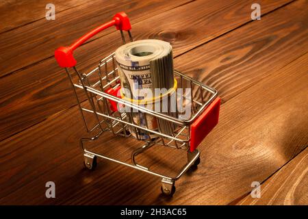 Black Friday Konzept. Geldwade im Warenkorb. US-Dollar in einem kleinen Metall-Einkaufswagen auf einem schönen braunen Holzhintergrund. Bereit Stockfoto