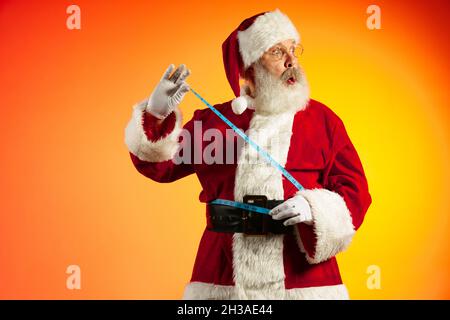 Emotionaler älterer Mann, der Weihnachtsmann posiert isoliert auf rot gelbem Hintergrund in Neon. Gesundes Neues Jahr 2022 Stockfoto