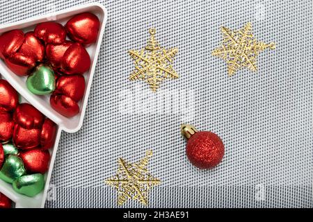 Herzförmige Schokoladen-Bonbons auf einem kieferförmigen Teller mit Weihnachtsdekorationen auf metallischem Silberblech-Hintergrund. Stockfoto