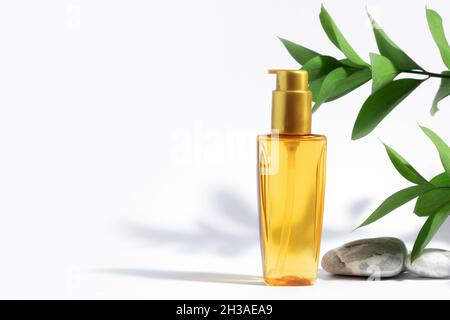 Klare Flasche gelbes Orangenöl für Sonnenschutz, Bräunung oder Haare. Weißer Hintergrund mit harten Schatten, Pflanzen und Steinen. Pflegekosmetik im Sommer. C Stockfoto