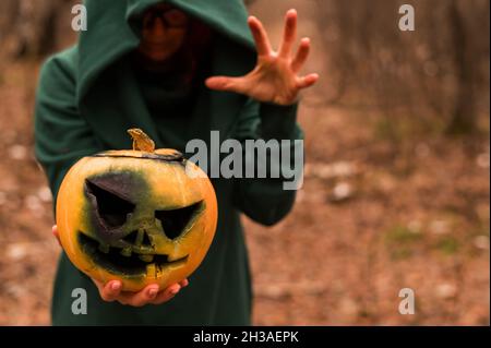 Eine gruselige Hexe hält einen dampfenden Kürbis in einen tiefen Wald. Jack o Laterne strahlt für halloween gelben Rauch aus Stockfoto