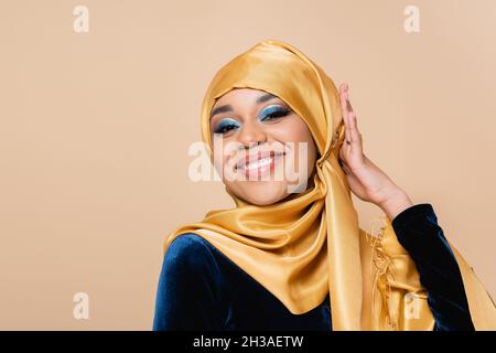 Fröhliche muslimische Frau, die gelben Hijab auf Beige einstellt Stockfoto