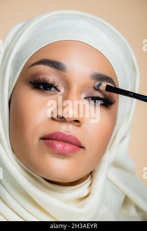 Nahaufnahme einer jungen muslimischen Frau im Hijab, die einen auf Beige isolierten Lidschatten anwendet Stockfoto