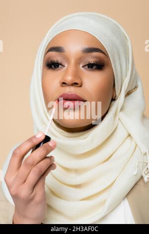 Junge muslimische Frau in Hijab, die Lippenglanz auf Beige isoliert anwendet Stockfoto