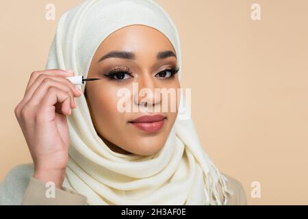 Junge muslimische Frau im Hijab, die schwarze Augenlinse auf Beige auftragen Stockfoto