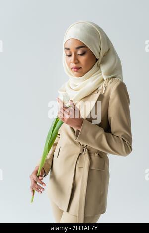 muslimische junge Frau in Hijab, die Tulpe isoliert auf Grau betrachtet Stockfoto