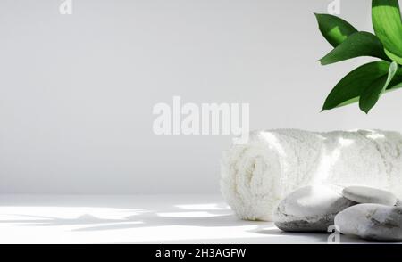 Spa-Hintergrundkonzept. Handtuch und Steine auf weißem Hintergrund mit harten Schatten, mit Blättern. Das Konzept der Körperpflege und Entspannung, Behandlung. Stockfoto