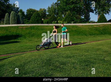 Laufsport Paar schieben Jogging Kinderwagen mit Kind im Park im Freien. Morgenlauf für die ganze Familie Stockfoto