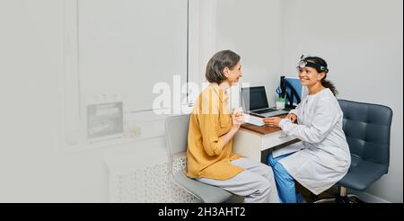 Reife Frau während der Konsultation mit HNO-Arzt in der medizinischen Klinik in Innenräumen. Behandlung der HNO-Erkrankung bei älteren Menschen Stockfoto