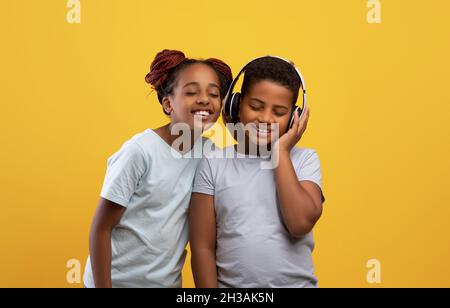 Emotionale schwarze Geschwister mit schnurlosen Headsets, die gemeinsam Musik hören Stockfoto