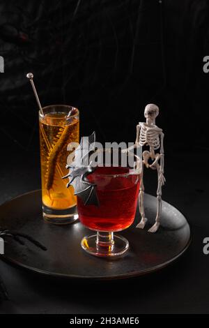 Halloween rot und orange alkoholische Cocktails verziert Fledermaus und Skelett auf schwarzem Hintergrund. Horror lustiges Getränk für festliche Party. Stockfoto