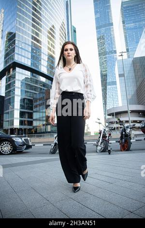 Junge Geschäftsfrau mit modernen Wolkenkratzern hinten in schwarzer Hose Stockfoto