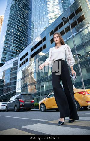 Seriöse junge Geschäftsfrau in der modernen Stadt der Skyscaper am Fußgängerübergang Stockfoto