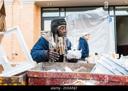 New York City, USA. Obdachloser afroamerikanischer Mann sucht einen Müllcontainer nach übrig gebliebenen Essensresten.aufgrund der wirtschaftlichen Umstände und des Rückgangs der psychischen Gesundheitsversorgung boomt die Zahl der Obdachlosen, die auf den Straßen leben. Stockfoto