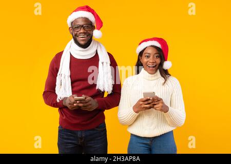 Afroamerikanisches Paar Hält Smartphones Tragen Santa Hüte, Studio Shot Stockfoto