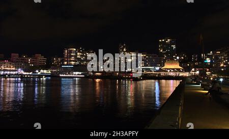 Wunderschöne Nachtansicht der Shipyards, einem Viertel im Norden von Vancouver, mit Menschen, die sich am Steg entspannen und beleuchtete Gebäude. Stockfoto