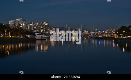 Atemberaubende Aussicht auf die Bucht von False Creek bei Nacht mit der beleuchteten Skyline von Vancouver Downtown, die sich im ruhigen Wasser mit dem Yachthafen und den Jachtbooten widerspiegelt. Stockfoto